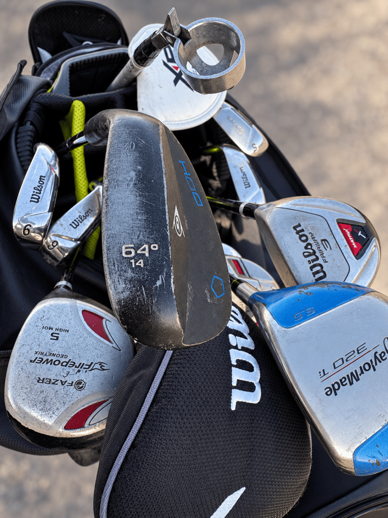 Brian's golf bag with old Wilson irons, a Wilson 3-wood, a Firepower 5-wood, a TaylorMade 320Ti driver and a black 64-degree wedge